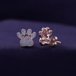 May include: A pair of rose gold paw print earrings with small diamonds set in the paw print design.