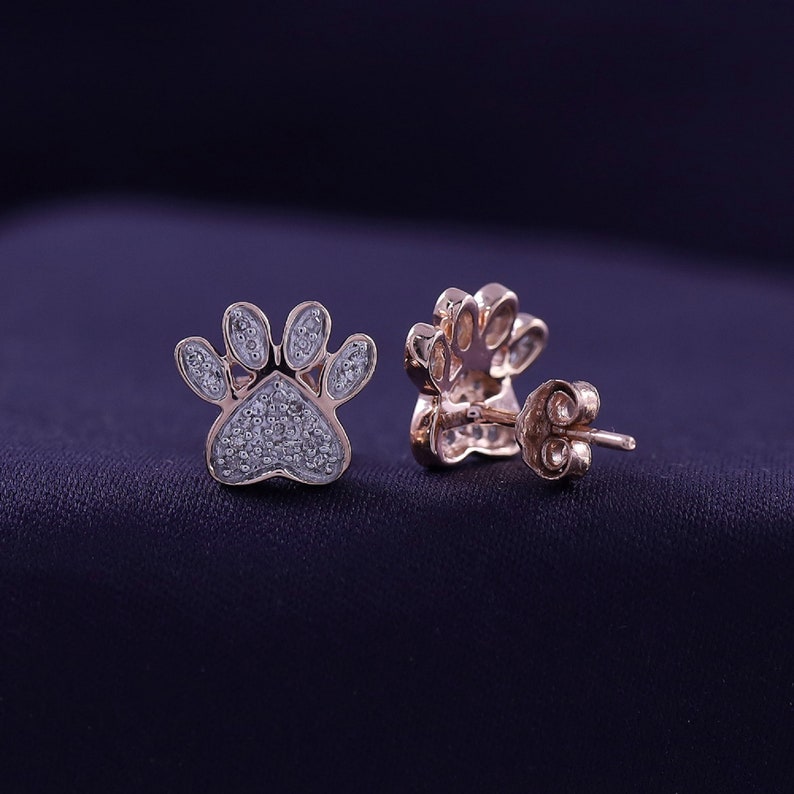 May include: A pair of rose gold paw print earrings with small diamonds set in the paw print design.