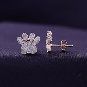May include: A pair of rose gold paw print earrings with clear cubic zirconia stones.