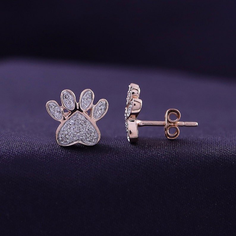 May include: A pair of rose gold paw print earrings with clear cubic zirconia stones.