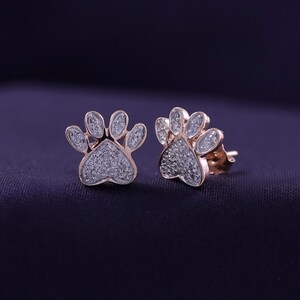 May include: A pair of rose gold earrings shaped like paw prints, each set with small sparkling diamonds.