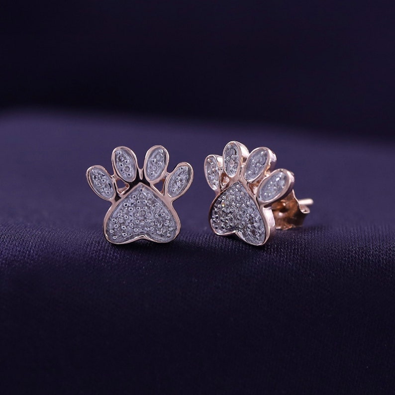 May include: A pair of rose gold earrings shaped like paw prints, each set with small sparkling diamonds.