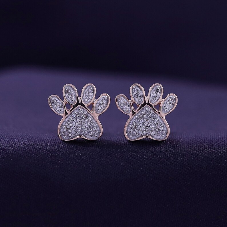 May include: A pair of rose gold paw print earrings with small diamonds set in the paw print design.