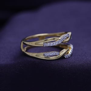 Op de afbeelding: Een gouden ring met een dubbelband ontwerp. De banden zijn met elkaar verweven en bezet met kleine, heldere stenen.