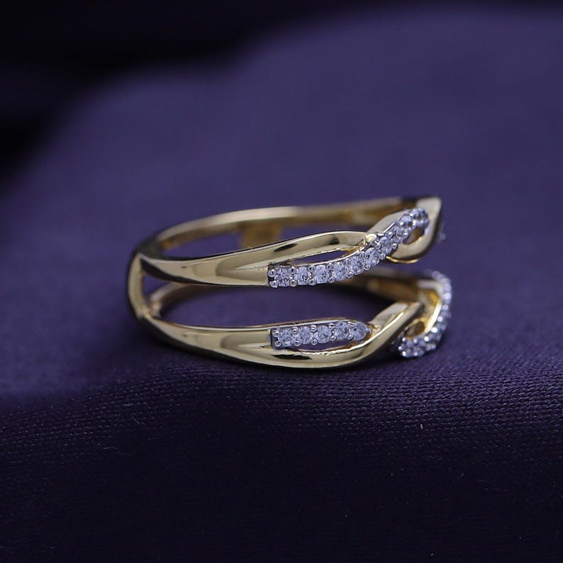 Op de afbeelding: Een gouden ring met een dubbelband ontwerp. De banden zijn met elkaar verweven en bezet met kleine, heldere stenen.