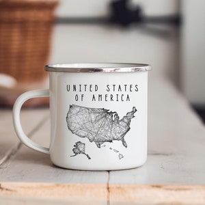 Könnte beinhalten: Weißer Emaillebecher mit silbernem Rand und Henkel. Der Becher zeigt den Text "UNITED STATES OF AMERICA" über einer schwarz-weißen Strichzeichnung der US-Karte.