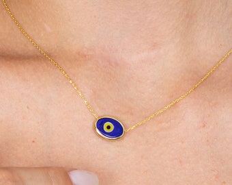 May include: A delicate gold necklace featuring a blue and yellow evil eye pendant. The pendant has a gold border and is suspended from a fine gold chain. The necklace is displayed on a person's neck.