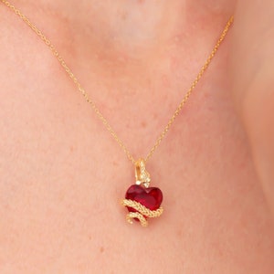 Peut inclure: Un collier doré avec un pendentif en forme de cœur rouge, orné d'un serpent doré. La chaîne fine en or contraste avec le cœur rouge, créant un bijou saisissant. Le design est élégant et original.