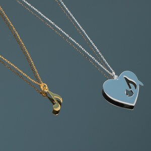 Puede incluir: Dos collares con temas musicales. Uno es dorado con un colgante de nota musical. El otro es plateado con un colgante en forma de corazón con una nota musical recortada. Ambos collares tienen cadenas delicadas.