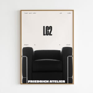 Könnte beinhalten: Gerahmtes Poster mit einem schwarzen LC2-Sessel-Design auf weißem Hintergrund. Das Poster zeigt den Text "LC2" in großen schwarzen Buchstaben, mit "designed by le corbusier" ebenfalls sichtbar. Der Rahmen ist hellbraun.