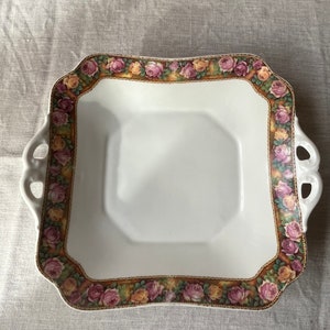 Peut inclure: Un plat de service carré blanc avec une bordure florale. La bordure présente des roses roses, jaunes et vertes avec des accents dorés.