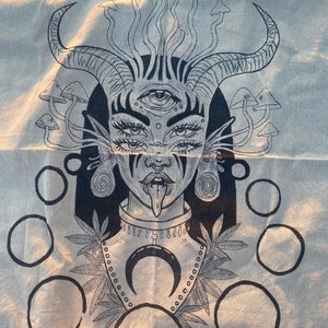 Puede incluir: Dibujo en blanco y negro de una persona con cuernos, un tercer ojo y la lengua fuera. La persona est&aacute; rodeada de setas y c&iacute;rculos. La persona lleva un collar con un colgante de media luna.