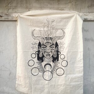 Puede incluir: Una ilustraci&oacute;n en blanco y negro de una mujer con cuernos, un tercer ojo y la lengua fuera. Est&aacute; rodeada de setas y c&iacute;rculos. La ilustraci&oacute;n est&aacute; impresa en un lienzo blanco.