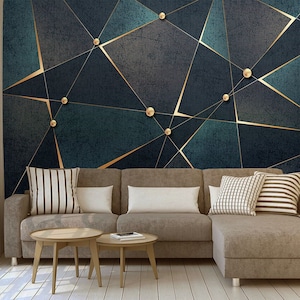 Può includere: Un divano angolare con rivestimento in tessuto marrone chiaro e una carta da parati geometrica con motivi blu scuro e oro dietro. Il divano ha tre cuscini, due a strisce bianche e marroni e uno di colore bianco pieno.