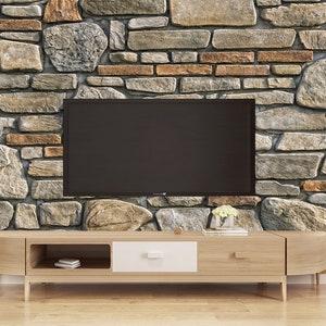 May include: A wooden TV stand with a white drawer and two open shelves. The stand is in front of a stone wall with a flat screen TV mounted on the wall.