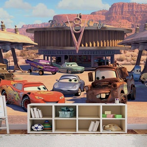 K&ouml;nnte beinhalten: Ein farbenfrohes Wandbild mit einer Tankstelle mit dem Text "Flo's V8 Cafe" und verschiedenen Cartoon-Autos, darunter ein rotes Rennwagen, ein blaues Auto, ein rostiger Abschleppwagen und ein gr&uuml;ner Van.