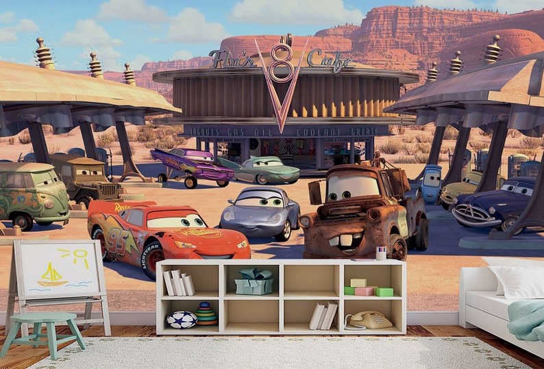 K&ouml;nnte beinhalten: Ein farbenfrohes Wandbild mit einer Tankstelle mit dem Text "Flo's V8 Cafe" und verschiedenen Cartoon-Autos, darunter ein rotes Rennwagen, ein blaues Auto, ein rostiger Abschleppwagen und ein gr&uuml;ner Van.