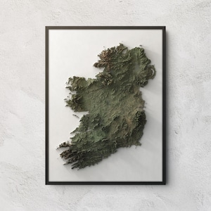 May include: A framed wall art piece featuring a three-dimensional topographic relief map of the island of Ireland. The map displays detailed terrain elevations in shades of deep green, brown, and tan, set against a plain white background.