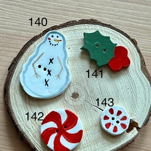 May include: Four holiday-themed buttons labeled 140, 141, 142, and 143. Button 140 is a white snowman, 141 is a green holly leaf with red berries, 142 is a large red and white peppermint swirl, and 143 is a small red and white peppermint.