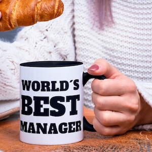 May include: White coffee mug with a black rim and handle. The mug has black text that reads "WORLD'S BEST MANAGER".