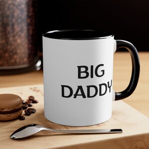 May include: White ceramic mug with a black rim and handle. The mug has the text "BIG DADDY" printed in black.