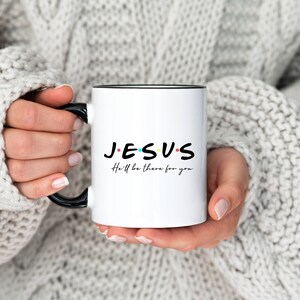 K&ouml;nnte beinhalten: Wei&szlig;e Keramiktasse mit schwarzem Rand und Henkel. Die Tasse tr&auml;gt die Worte "JESUS" in Schwarz mit bunten Punkten und den Text "He'll be there for you" in Schwarz darunter.