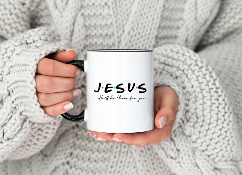 K&ouml;nnte beinhalten: Wei&szlig;e Keramiktasse mit schwarzem Rand und Henkel. Die Tasse tr&auml;gt die Worte "JESUS" in Schwarz mit bunten Punkten und den Text "He'll be there for you" in Schwarz darunter.