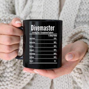 May include: Black ceramic coffee mug with white text that reads "Divemaster" and a list of qualities with percentage values. The qualities include hard work, dedication, passion, respect, knowledge, caffeine, and regret.