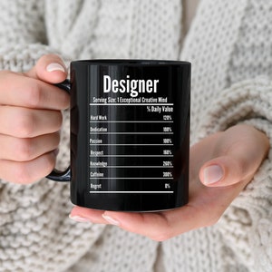 May include: Black coffee mug with white text that reads "Designer" and a chart listing the percentage daily value of hard work, dedication, passion, respect, knowledge, caffeine, and regret.