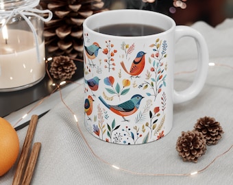 May include: White ceramic mug with a colorful floral pattern featuring birds. The mug is filled with a dark brown liquid and has a white handle.