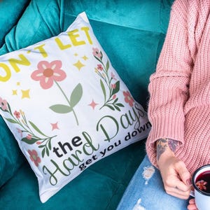 May include: White throw pillow with a floral design and the text "Don't let the hard days get you down".