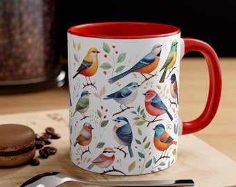 May include: A white ceramic mug with a red rim and handle. The mug features a colorful pattern of birds and leaves on a white background.