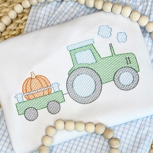 May include: A green tractor with a blue and white tire pulls a wagon with a single orange pumpkin. The tractor has a white cab and a black exhaust pipe. The wagon has a green bed and black wheels.
