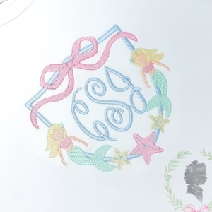 Könnte beinhalten: Weißer Baby-Strampler mit einem hellblauen, rosa und grünen gestickten Monogramm, umgeben von Meerjungfrauen und Seesternen. Der Strampler hat einen Rüschen am Ausschnitt und der Text "Sweet Shiloh Baby + Child" steht auf dem Etikett.