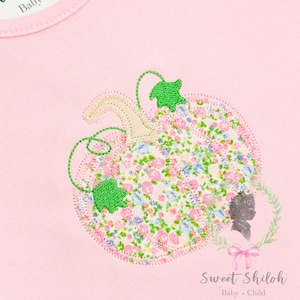 Pode incluir: Macacão rosa para bebê com um design de abóbora floral e o texto "Sweet Shiloh Baby + Child" na etiqueta.