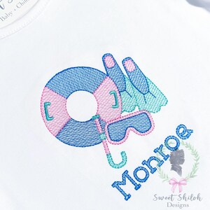 May include: Embroidered design of a blue and pink life preserver, blue and pink goggles, and blue and green flippers with the name "Monroe" in blue embroidery.
