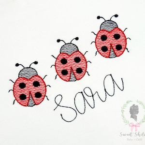 May include: Embroidered design featuring three red ladybugs with black spots and antennae. The name "Sara" is written in cursive below the ladybugs. A logo with a silhouette and text is in the bottom right corner.