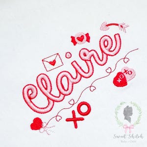 May include: Embroidered design featuring the name "Claire" in a cursive font, accompanied by Valentine's Day themed elements. Includes a candy, an envelope with a heart, an arrow, and hearts. The design is in red and pink on a white background.