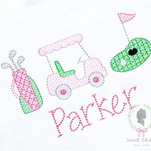 Könnte beinhalten: Gesticktes Design mit Golf-Motiv, einschließlich einer Golftasche, einem Golfwagen und einem Golfball mit Fahne. Das Design ist in Rosa und Grün gehalten, mit dem Namen "Parker" in rosa Schrift. Das Logo "Sweet Shiloh Baby + Child" ist ebenfalls vorhanden.