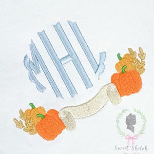 May include: An embroidered design on white fabric featuring the light blue monogram letters MHL. Below the letters is a beige ribbon banner flanked by two clusters of orange pumpkins and tan leaves. A small logo with a silhouette is in the corner.