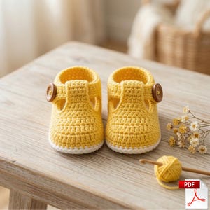 May include: Handmade yellow crochet baby shoes with white trim and wooden button fastenings. The shoes are displayed on a wooden surface, highlighting the detailed crochet pattern. A PDF icon is visible in the bottom right corner.