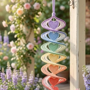 May include: A hanging spiral decoration made of crocheted yarn featuring a vertical sequence of seven hearts in a rainbow gradient of colors including purple, blue, green, yellow, orange, and red, suspended from a light purple yarn loop.