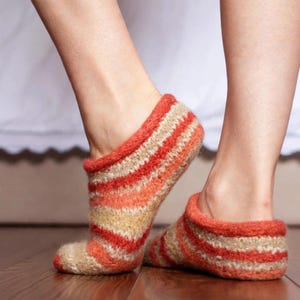 May include: A pair of low-cut ankle socks featuring a textured knit pattern with horizontal stripes in shades of vibrant orange, soft peach, and beige. The socks have a thick, rolled-style cuff at the opening and a fuzzy, soft-touch appearance.