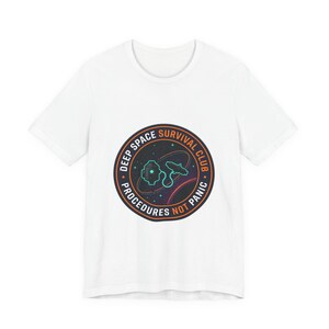 May include: White t-shirt with a circular graphic that reads "DEEP SPACE SURVIVAL CLUB". The graphic features a space-themed design with planets, stars, and a spaceship. The words "PROCEDURES NOT PANIC" are also included in the design.