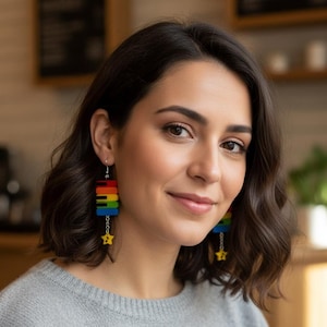 May include: A pair of earrings with a rainbow piano key design. The earrings are made of stacked rectangular blocks in red, orange, yellow, green, blue, and purple. Each earring has a small yellow star charm hanging from a chain.
