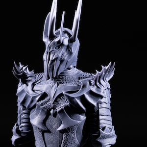 Puede incluir: Una figura detallada, gris, impresa en 3D de un personaje que lleva un casco con una corona y una armadura adornada. El casco tiene una corona puntiaguda y una m&aacute;scara facial con detalles intrincados.