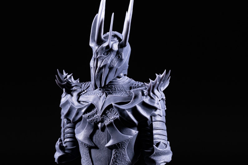 Puede incluir: Una figura detallada, gris, impresa en 3D de un personaje que lleva un casco con una corona y una armadura adornada. El casco tiene una corona puntiaguda y una m&aacute;scara facial con detalles intrincados.