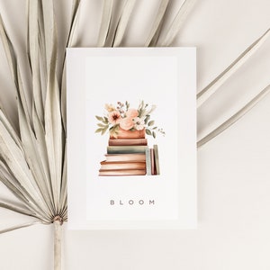 May include: A watercolor illustration of a stack of books with a bouquet of pink and white flowers on top. The text "BLOOM" is printed below the books.