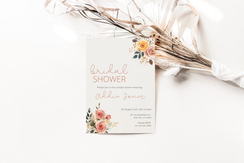 May include: A white card with a floral design and the text "bridal shower" in pink script. The card also includes the text "Please join us for a bridal shower honoring Addie Jones" and details about the event.