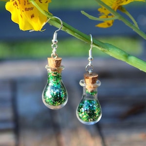 May include: A pair of silver dangle earrings with small glass bottles filled with green glitter and cork stoppers.